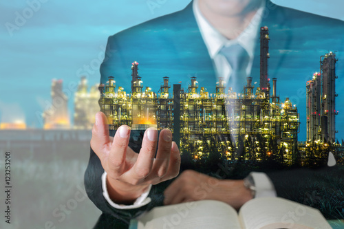 Double exposure of business man hand hold and oil refinery industry plant, Electric Generating Factory at night as Energy and Business success concept.