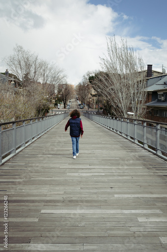 Girl walking in the footbridge in the city with wooden floor and steel. Rear view