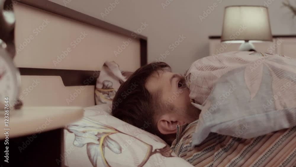 Frightened man hears something strange and hides under the blanket Frightened man hears something strange and hides under the blanket