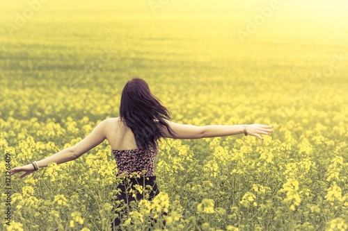 Beautiful genuine woman in sunny summer meadow from behind left. Attractive authentic young girl enjoying the warm summer sun in a wide green and yellow meadow. Part of series © azur13