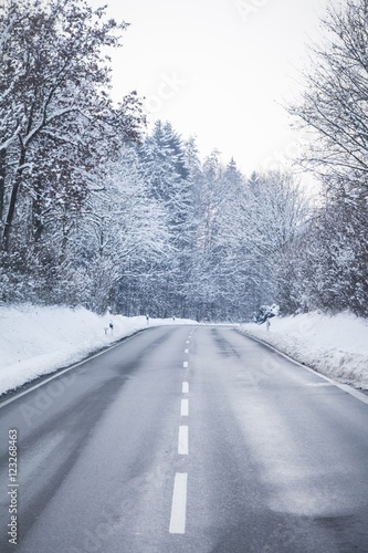 Cold winter road with wonderful white snow covered forest trees. The country street is wet and has a curcve in cold colors