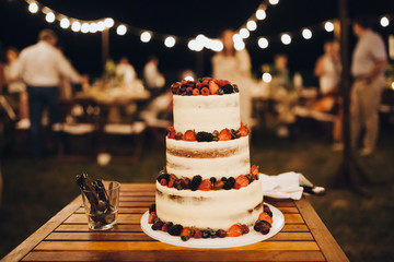 three-level white wedding cake decorated with cream and berries, stands on a table in the banquet area