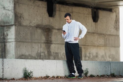 Attractive young man is preparing to exercise outdoors. He is looking for music suitable for running on his smart phone.