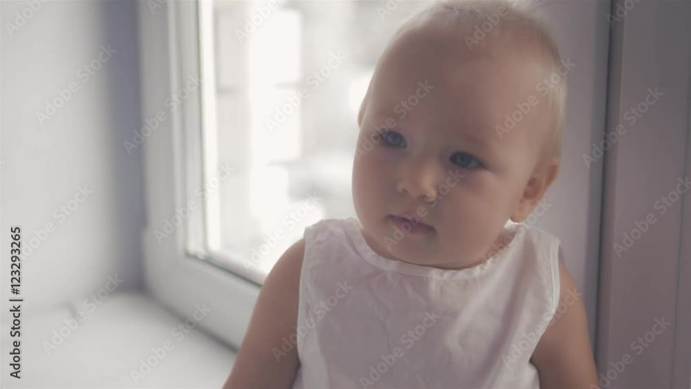 Cute little baby girl looking into the camera and seat near window Cute little baby girl looking into the camera and seat near window