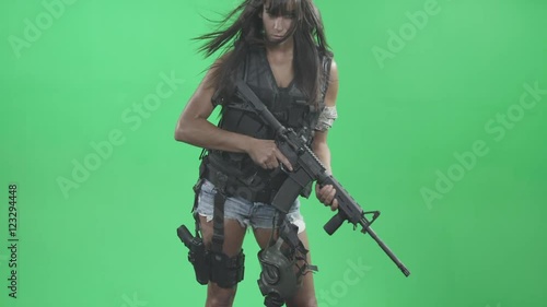  A woman solider standing with a gun and her hair blowing in the wind on a green screen.