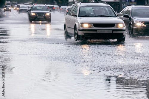 cars driving on a flooded city road with lights on during heavy rain