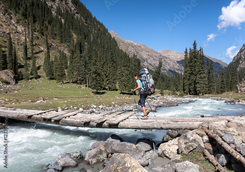 Hiker crossing river at mountains.