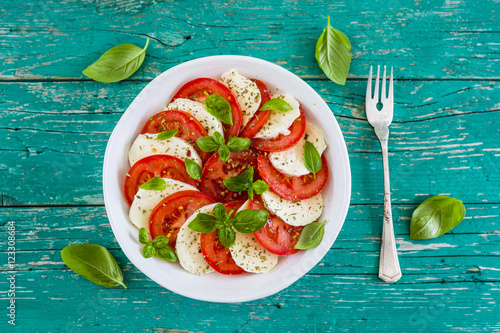 Delicious caprese salad with ripe tomatoes and mozzarella cheese with fresh basil leaves. Italian food.  photo