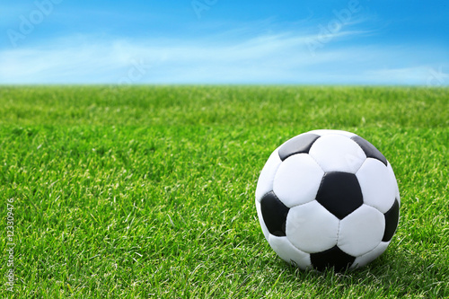 Soccer ball on green grass and blue sky background