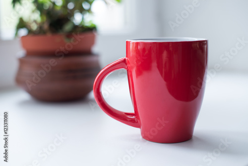 Red mug with tea or coffee on white table by the window