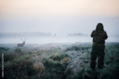 Hunter holding a rifle and aiming red deer prey in the mist  hunter photoshooting at the morning.