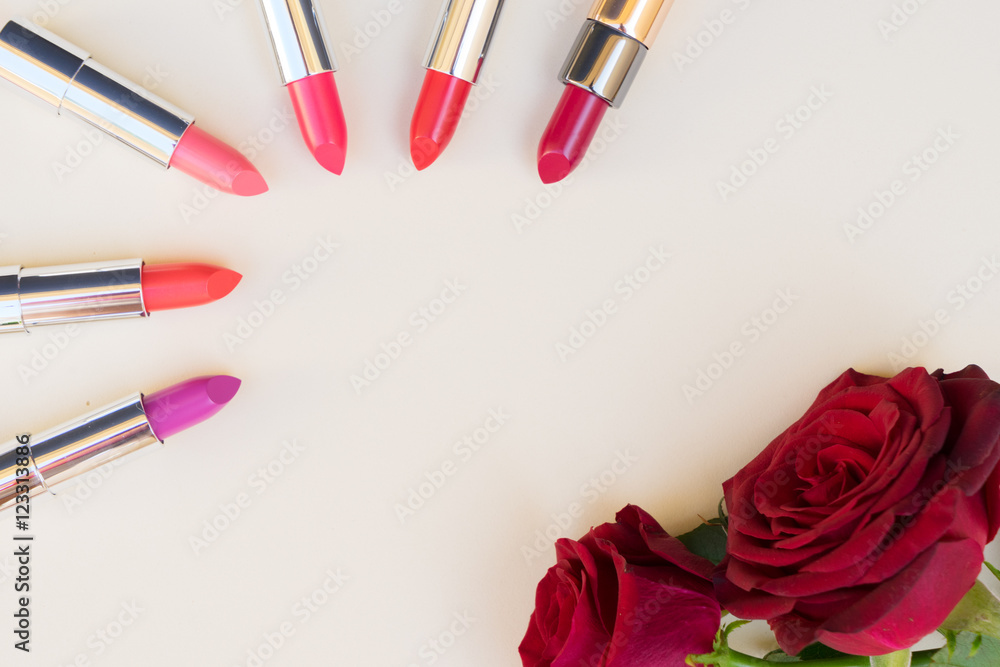 Obraz premium Collection of puple, pink and red shiny lipsticks and red roses, top view with copy space