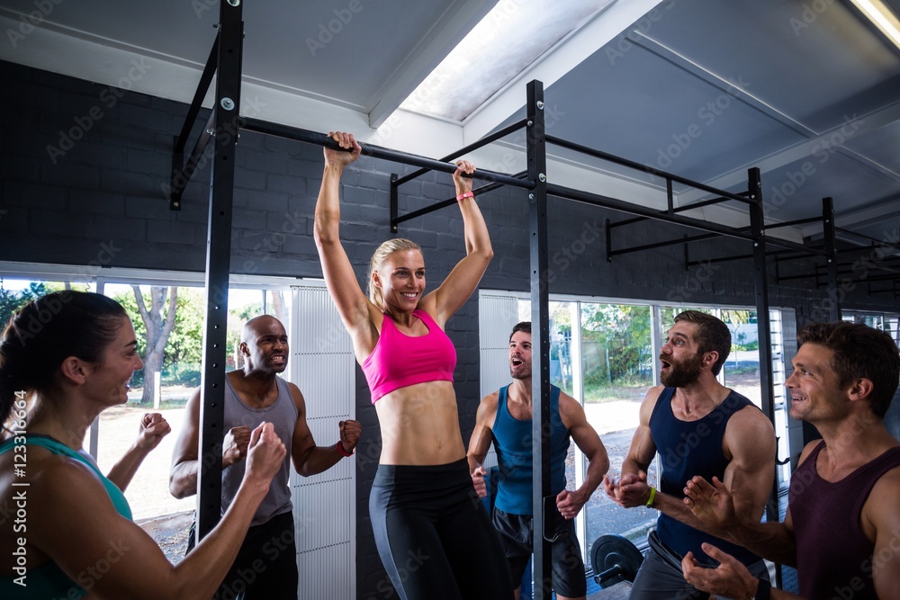 Smiling friends cheering woman doing chin-ups in gym Smiling friends cheering woman doing chin-ups in gym