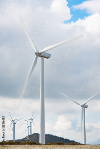 Wind turbines farm in eolic park generating energy with air flow with spinning blades in a rural setting. Clean renewable green wind power concept.