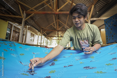Man making a batik by brushing hot wax on cloth, Jember, East Java, Indonesia photo
