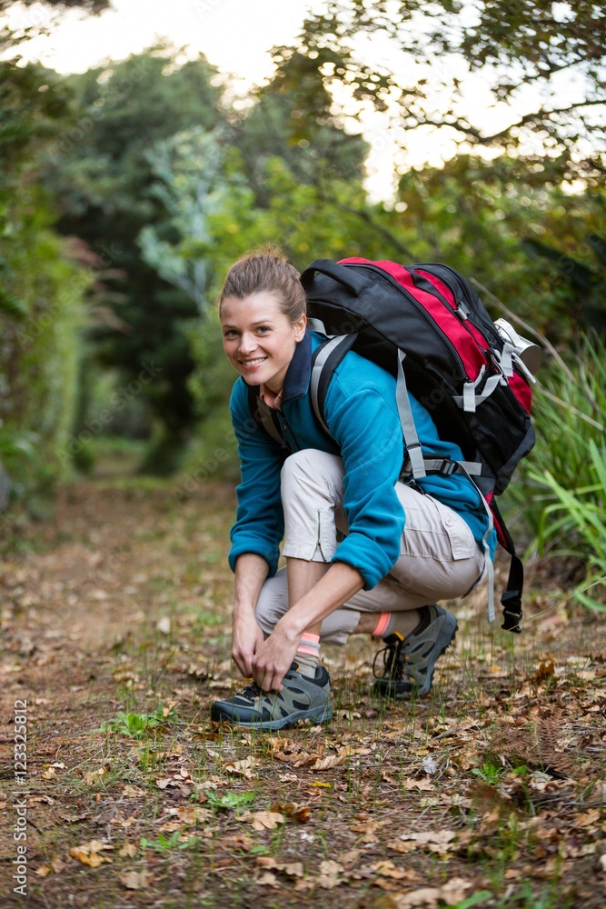 Smiling female hiker tying shoelaces in forest Smiling female hiker tying shoelaces in forest