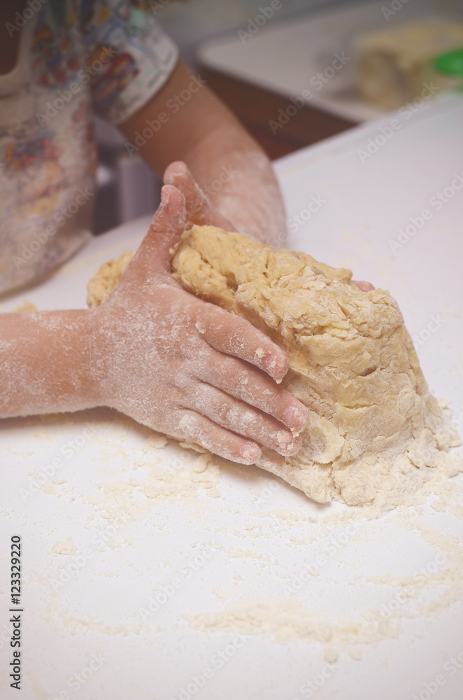 Vintage tonned photo with kid kneading the dough. Child helps to cook tasty cookies