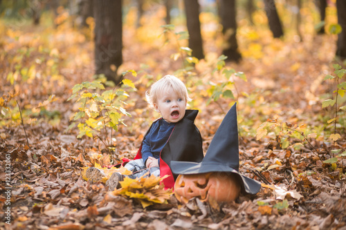 Halloween baby boy. Child in autumn forest looking at the falling leaves.