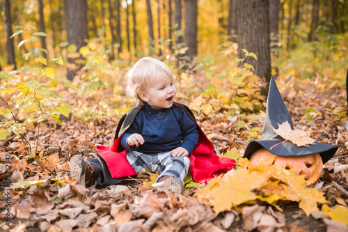 Halloween baby boy. Child in autumn forest looking at the falling leaves.