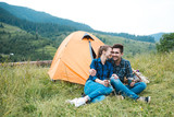 A couple of tourists in time of the hike, sit outside the tent, mountain scenery. The guy hugs the girl. The concept of love and recreation