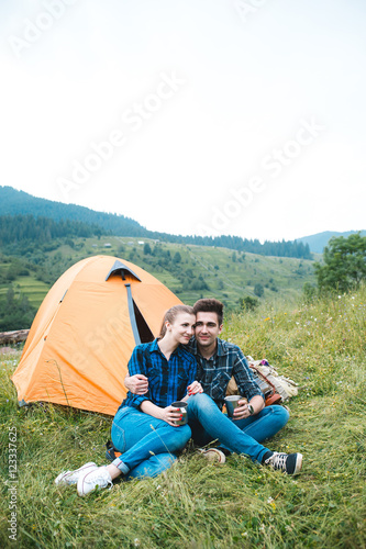 A couple of tourists in time of the hike, sit outside the tent, mountain scenery. The guy hugs the girl. The concept of love and recreation