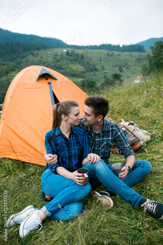 A couple of tourists in time of the hike, sit outside the tent, mountain scenery. The guy hugs the girl. The concept of love and recreation