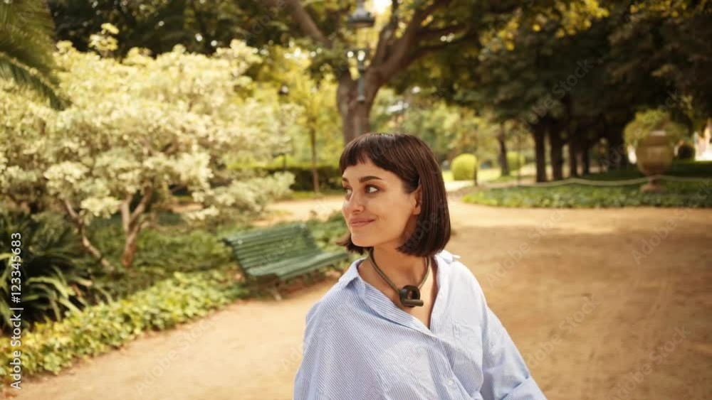 Happy smiling attractive brunette walks in park, looking at camera and sits on wooden park bench Happy smiling attractive brunette walks in park, looking at camera and sits on wooden park bench