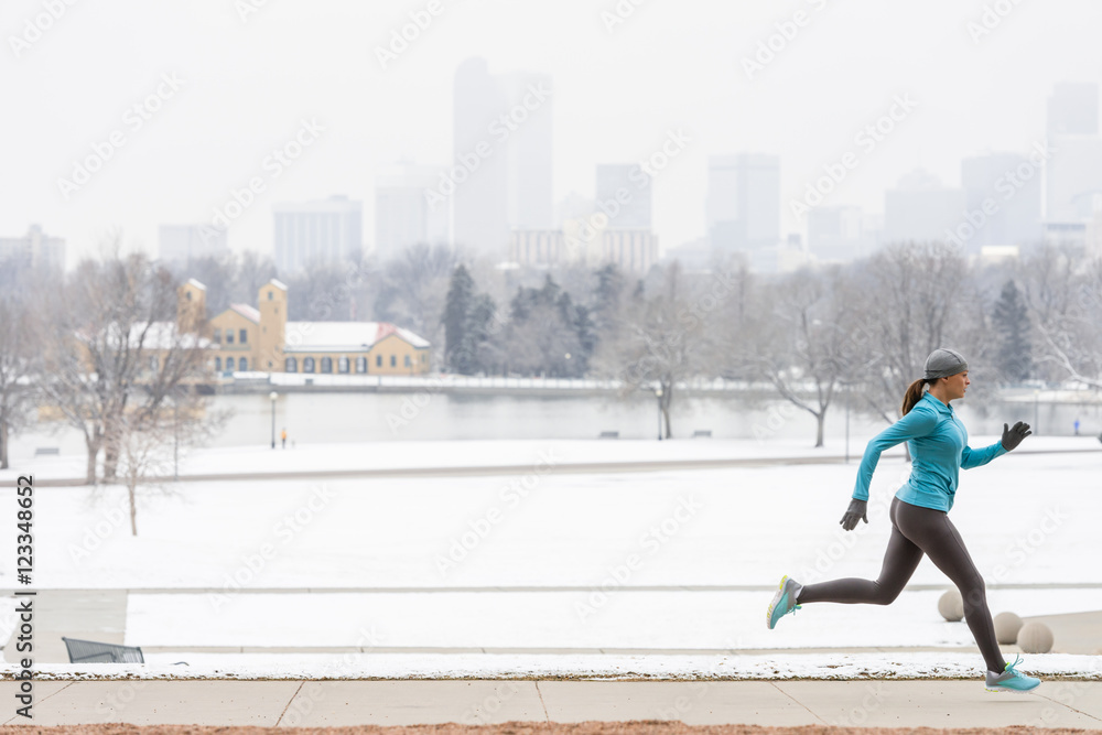 Woman running in winter through Denver Colorado City Park with skyline boathouse and snow in background Woman running in winter through Denver Colorado City Park with skyline boathouse and snow in background
