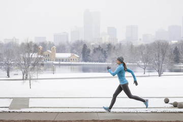 Woman running jogging exercising in snowy winter City Park with Denver Colorado skyline looming in background