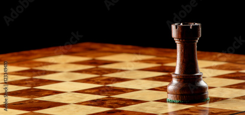 Carved wooden black rook castle chess piece on chessboard with dramatic lighting and black background