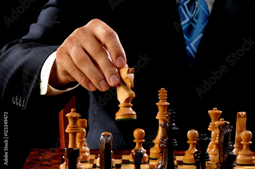 Close up of man in suit and tie moving carved wooden white knight in chess game with moody dark lighting