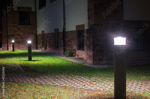Outdoor lights (lanterns, bollards) in front of an old administration building illuminating a walkway in the garden at night  photo