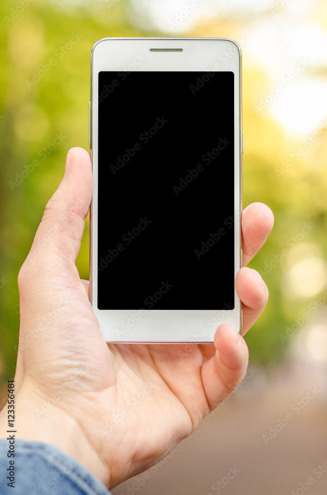 close up white mobile phone in hand a young hipster business man in on the background of green natural  grass and autumn leaves 