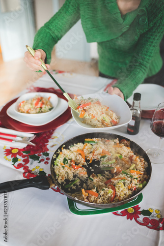 Close up on the hand of young handsome girl serving rice and vegetables from a pan to a plate using perforated spoon for chrismas meal - food  meal  veggie concept