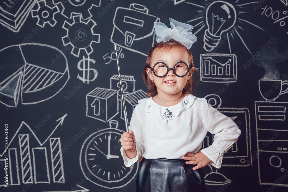 The little smart girl in glasses holding a pointer on dark background with business or school picture The little smart girl in glasses holding a pointer on dark background with business or school picture