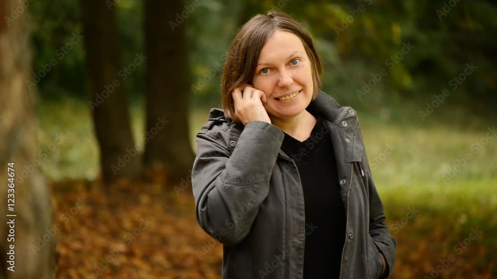 Beautiful young adult woman talking on smartphone in autumn park. Alone female using mobile phone for conversation, handheld shot through woods with selective focus. Beautiful young adult woman talking on smartphone in autumn park. Alone female using mobile phone for conversation, handheld shot through woods with selective focus.