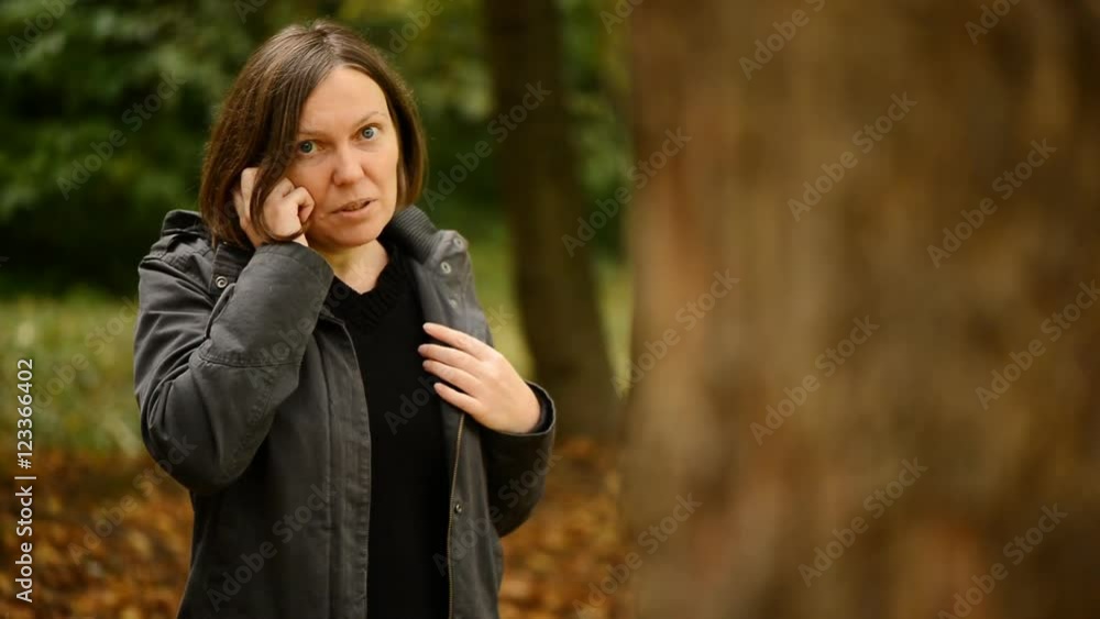 Beautiful young adult woman talking on smartphone in autumn park. Alone female using mobile phone for conversation, handheld shot through woods with selective focus. Beautiful young adult woman talking on smartphone in autumn park. Alone female using mobile phone for conversation, handheld shot through woods with selective focus.