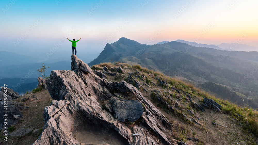 Fototapeta premium Winner man on peak of rocks mountain Hike at sunset, Active life