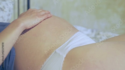 Young pregnant woman lying in bed and rubbing her belly photo