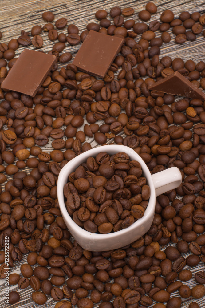 Fototapeta premium small white cup with coffee beans on wooden background