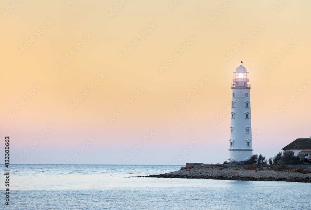 Lighthouse searchlight beam near ocean at sunset