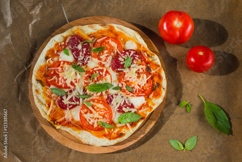 Homemade pizza with tomatoes, pepperoni and basil on craft paper background 