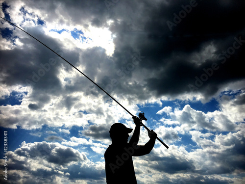 Silhouette of fisherman throwing fishing rod in lake