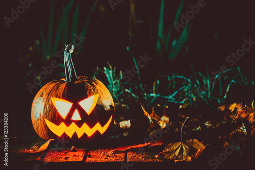 Glowing pumpkin symbolizing the head of old Jack, with autumn leaves night in a spooky dark background. Soft focus. shallow DOF