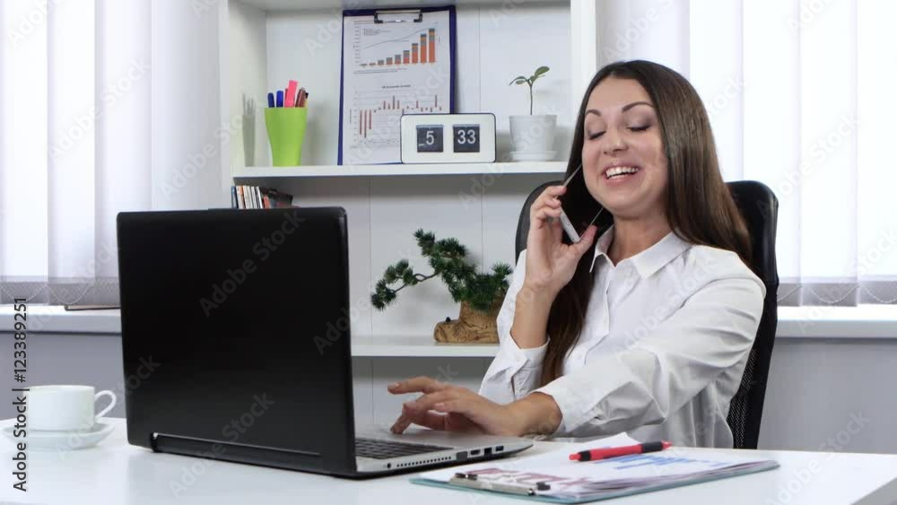 Business woman sitting in the office in front of a laptop and talking on the phone Business woman sitting in the office in front of a laptop and talking on the phone