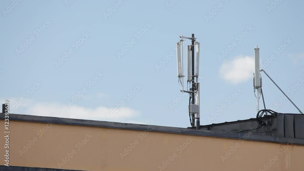 Mobile antenna on a residential building roof with some clouds passing at background. Mobile antenna on a residential building roof with some clouds passing at background.