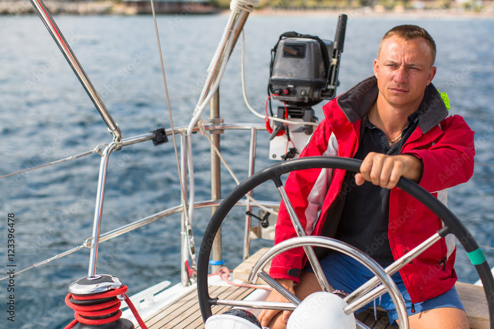 Naklejka premium Skipper at the helm controls of a sailing yacht.