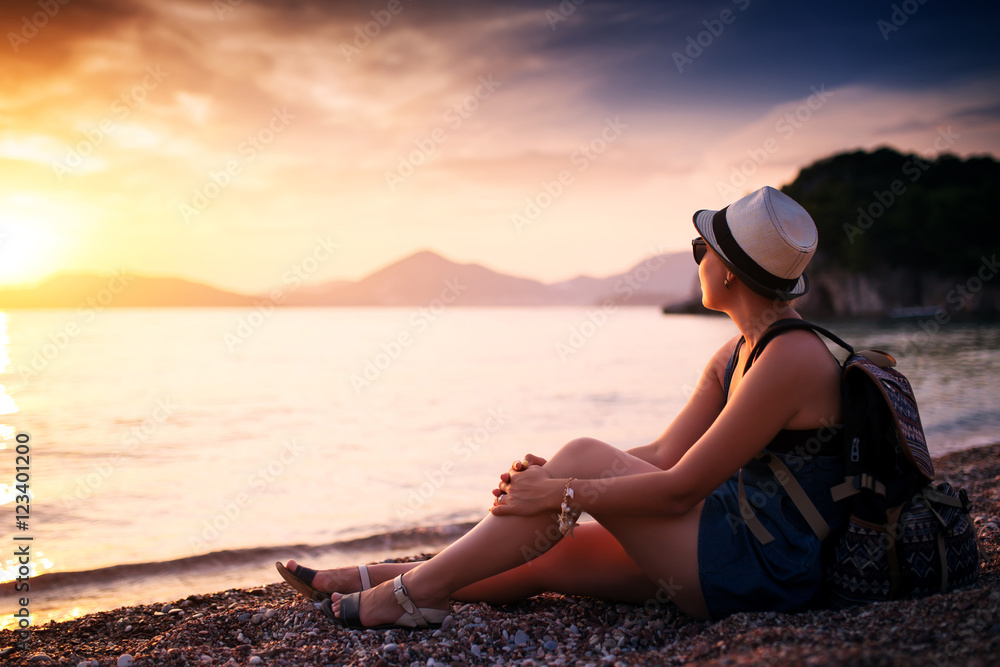 Woman sitting on pebble beach near sea at sunset