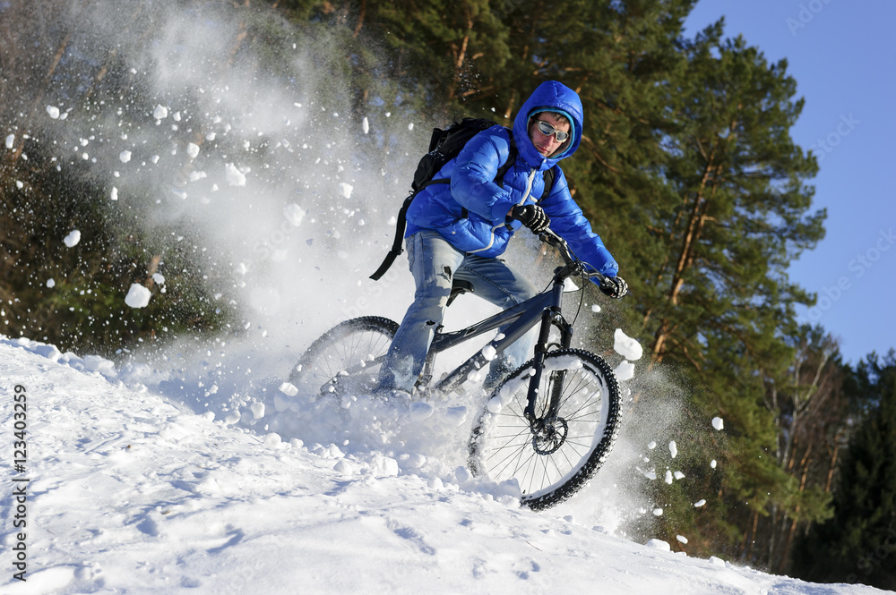 Obraz premium Cyclist riding bike, extreme winter cycling near snowbanks of snowy mountain slope, cross country biking near forest in cool sunny day 