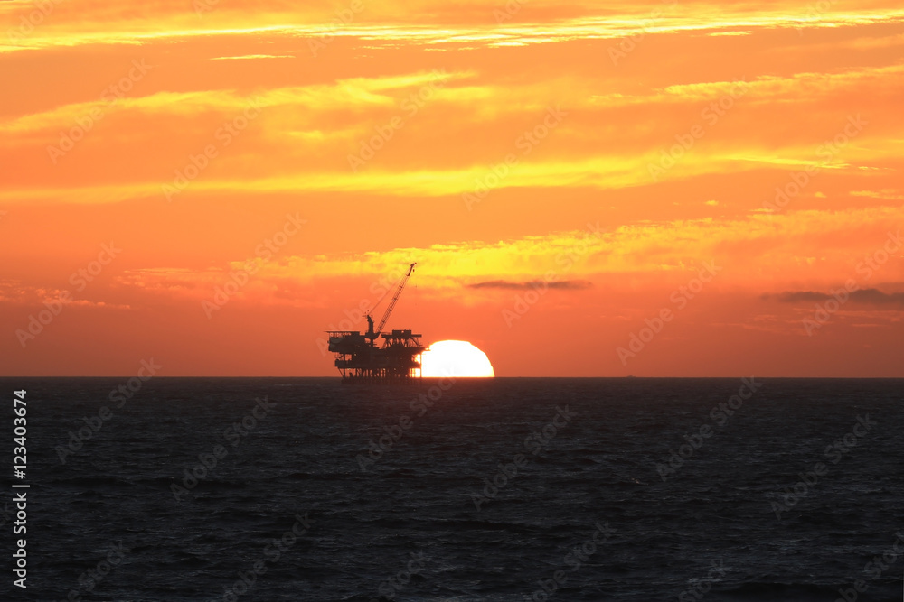 Beach off-shore oil rig platform at sunset